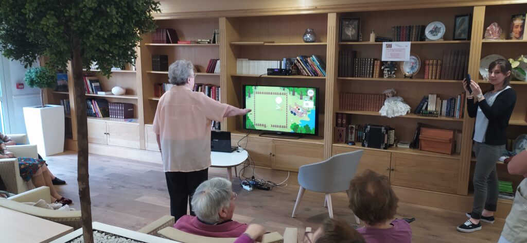 Photo d'une séance d'activité physique adaptée interactive avec des seniors utilisant MediMoov sur grand écran dans un salon bibliothèque